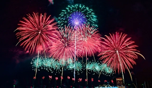 熱海海上花火大會夜晚煙火綻放，紅色、粉色與綠色大型煙火照亮海灣上空