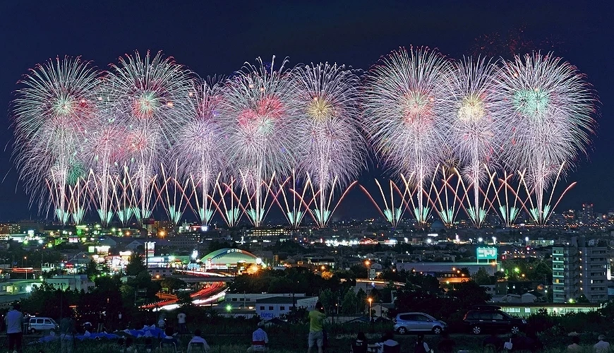 長岡花火大會夜景,大量煙火在信濃川上空同時綻放,前景為長岡市區與觀賞人群,呈現寬廣且密集的煙火畫面