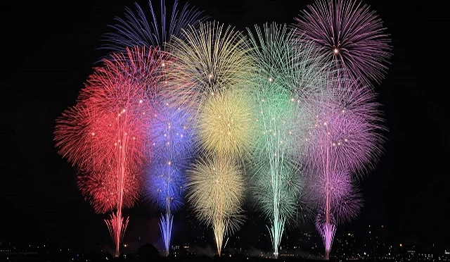 長岡花火大會夜景,多種顏色煙火在夜空同時綻放,下方為城市燈光與施放點,畫面色彩豐富且分布均勻