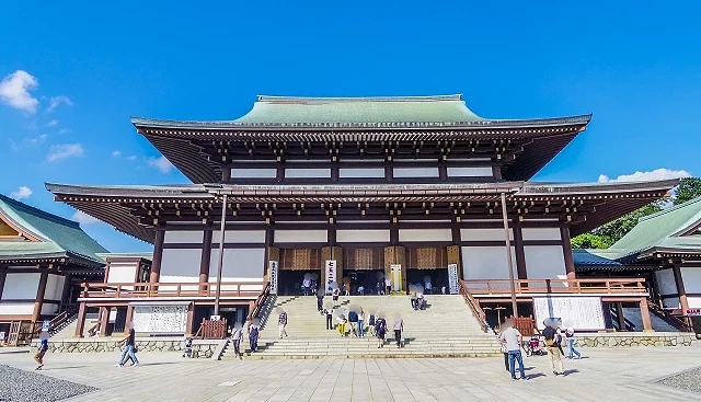 成田山新勝寺大本堂正面,遊客沿著石階前往參拜,寺院建築在晴朗藍天下十分壯觀