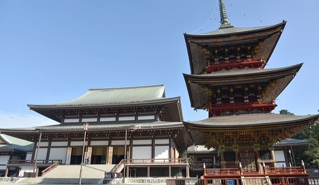 成田山新勝寺大本堂旁的三重塔,紅色塔身裝飾華麗,與寬闊寺院建築一同矗立在晴朗天空下
