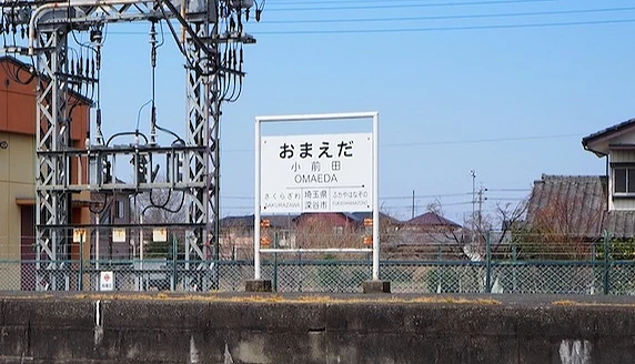 日本小前田车站(OMAEDA)月台站名牌,前方可见铁轨,背景为住宅与电线架