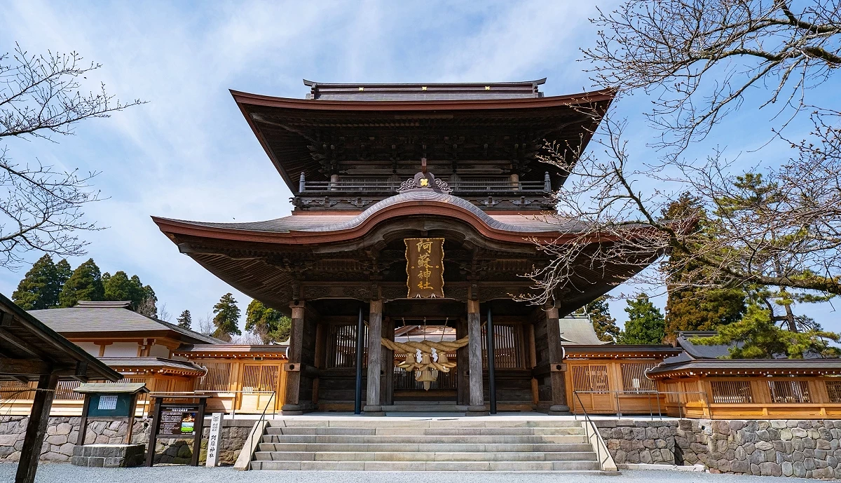 熊本縣阿蘇神社的木造樓門，正面懸掛注連繩，兩側可見石牆與境內建築。