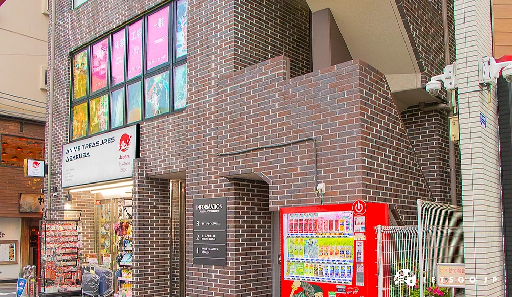 ANIME TREASURES ASAKUSA 深色磚牆建築的一樓為動漫精品店,門口設有紅色販賣機與樓層導覽牌。