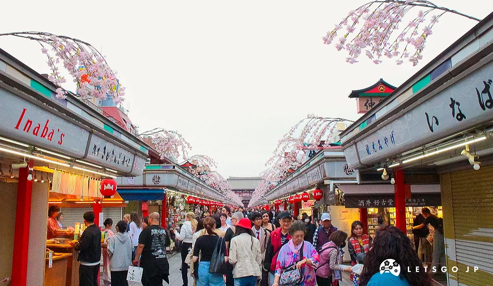 仲見世商店街 仲見世通商店街街道兩側林立紀念品店,上方裝飾著粉色花卉,遊客絡繹不絕