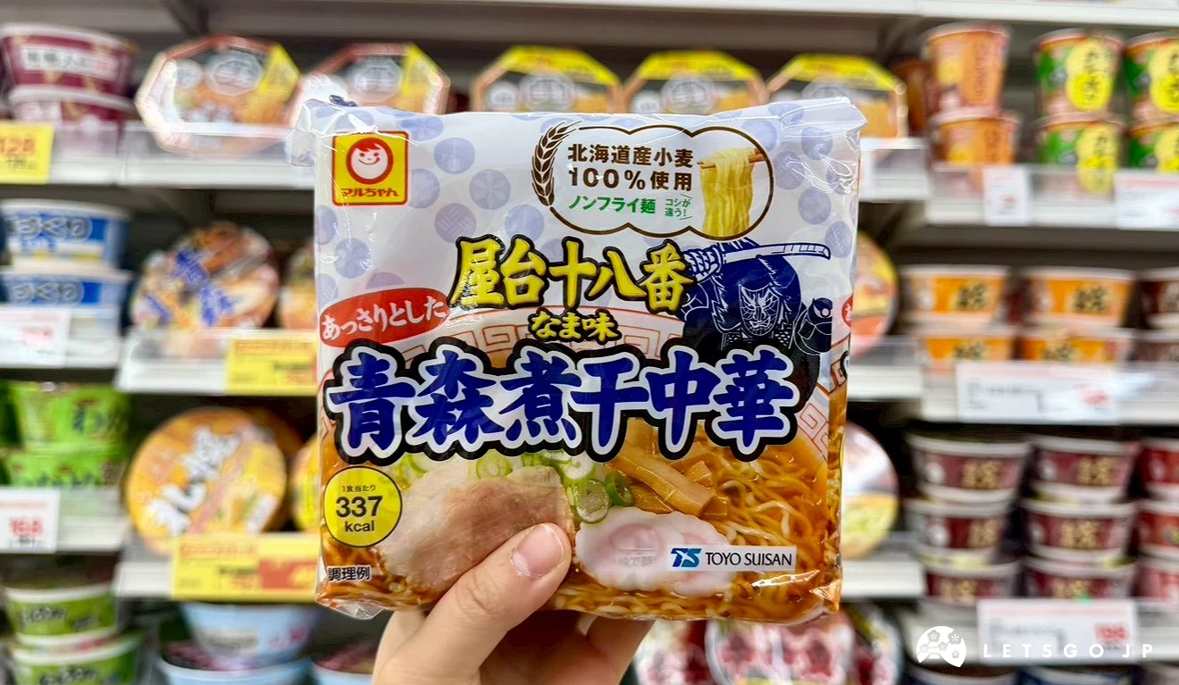 一隻手拿著一包東北限定的「青森煮干中華拉麵」黃色包裝袋,背景為店內的泡麵商品區。