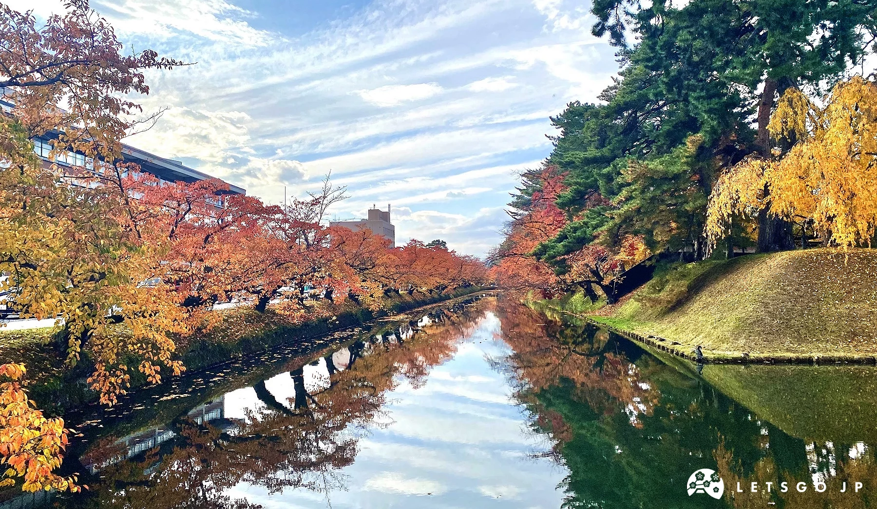 弘前公園護城河畔滿開的紅葉倒映在清澈水面上,呈現秋季楓紅延伸的對稱美麗景致。