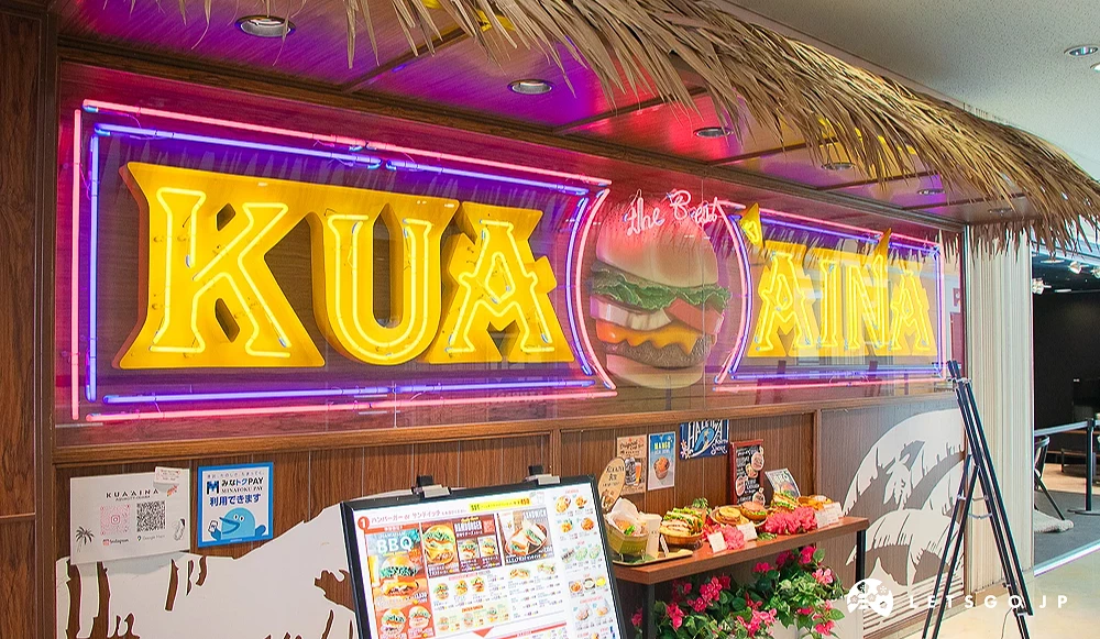 KUA`AINA 漢堡店門面 KUA`AINA 餐廳外觀設有黃色霓虹燈品牌字樣,上方覆蓋茅草裝飾。