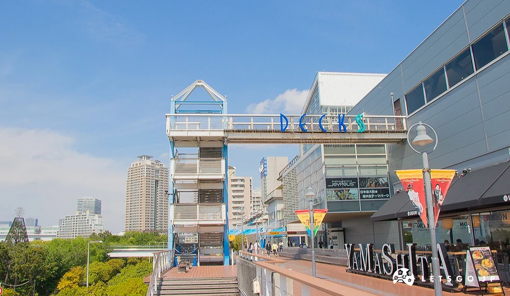 DECKS 東京海濱購物中心 DECKS 商場戶外木棧道,上方有天橋連接建築,遠方可見住宅大樓。