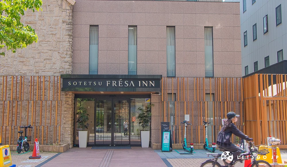 相鐵 FRESA INN 飯店大門 SOTETSU FRÉSA INN 咖啡色磚牆入口,前方有一名騎單車的行人經過。