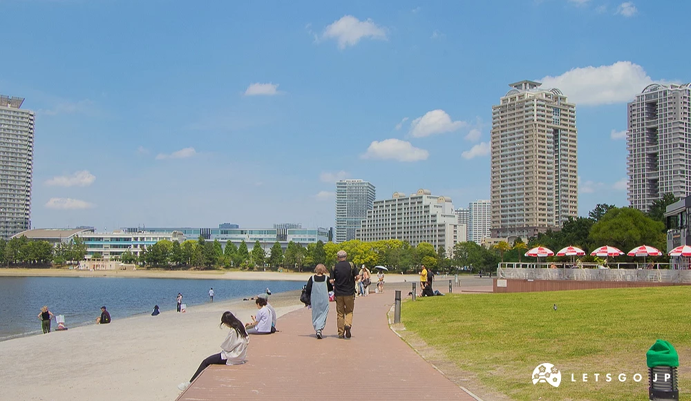 台場海濱公園海灘 行人走在海濱公園木棧道,左側為沙灘與海面,右側為草坪與大樓。