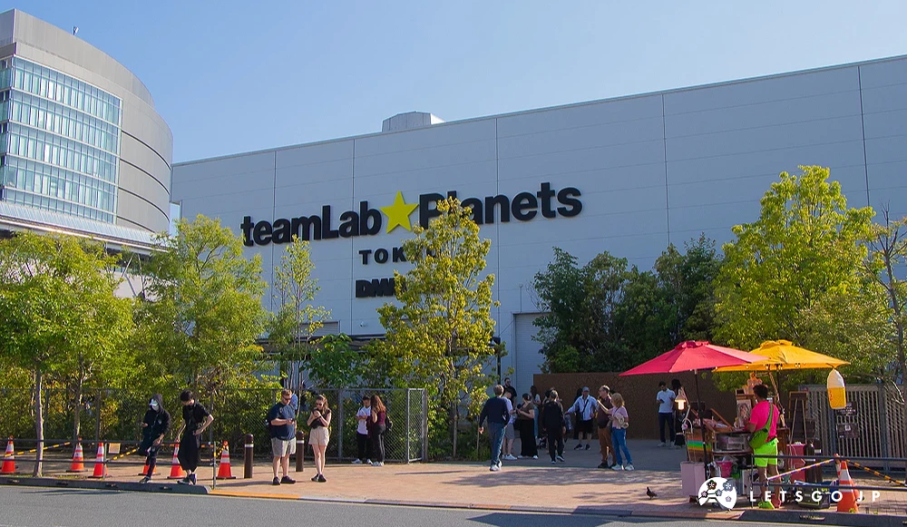 teamLab Planets 展館入口 teamLab Planets TOKYO 白色建築外牆,前方有路燈與排隊等候進場的遊客。