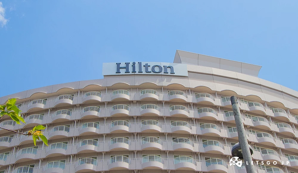 希爾頓飯店圓弧大樓 希爾頓酒店圓弧形外牆大樓,頂端設有「Hilton」品牌招牌,背景為藍天。