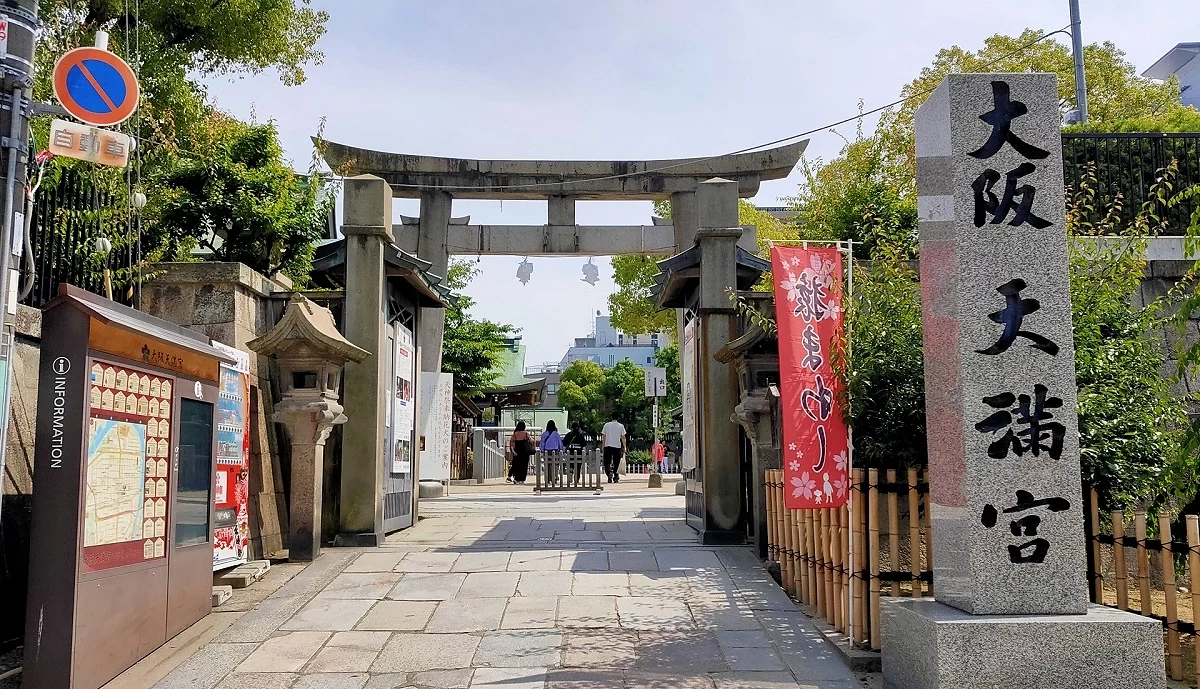 大阪天滿宮石鳥居與入口步道，右側石碑寫有神社名稱，參拜者沿著石板路進入境內