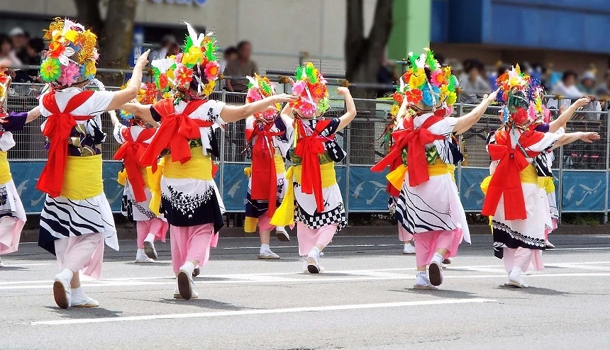 多位身穿传统服饰与彩色花笠的舞者于街道上表演日本祭典舞蹈,呈现热闹缤纷的夏季祭典景象