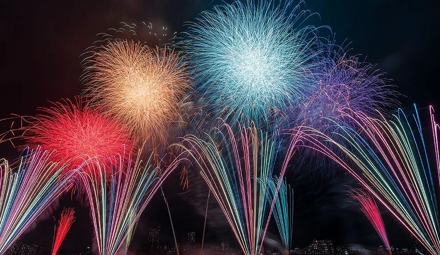 江戶川區花火大會夜空中綻放紅色、金色、藍色與粉色大型煙火，下方有多道彩色光束向上升起