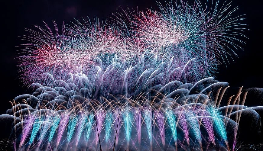 江戶川區花火大會夜空中施放大量藍綠色、粉紅色與白色煙火，形成層次豐富的連發畫面