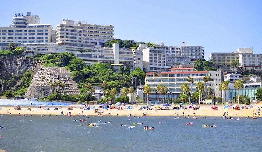 海水浴場前的海岸線與溫泉飯店群，沙灘上聚集戲水與休憩遊客