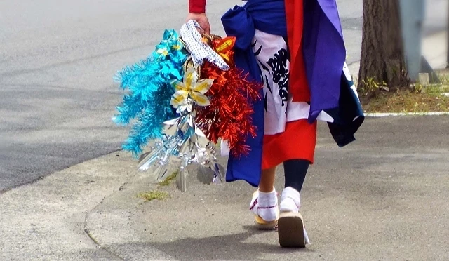 身穿日本传统祭典服饰的参加者手持色彩鲜艳花笠装饰走在街道上,展现地方祭典准备氛围