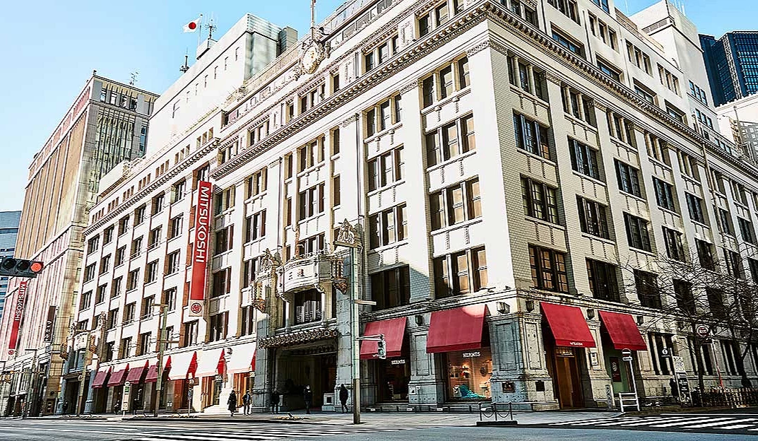 一棟六七層樓高建築,一樓的店鋪上面有紅色屋簷