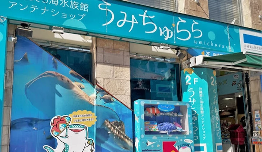 沖繩美麗海水族館官方周邊商店「うみちゅらら」外觀,寫有日文標語,櫥窗貼有鯨鯊圖案與吉祥物立牌