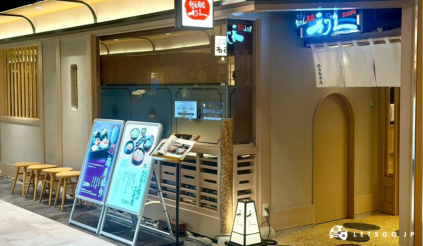 位於百貨街轉角的利久牛舌仙台站本店外觀,日式暖簾與木質裝潢搭配柔和燈光,門口擺放著精緻的菜單立牌。