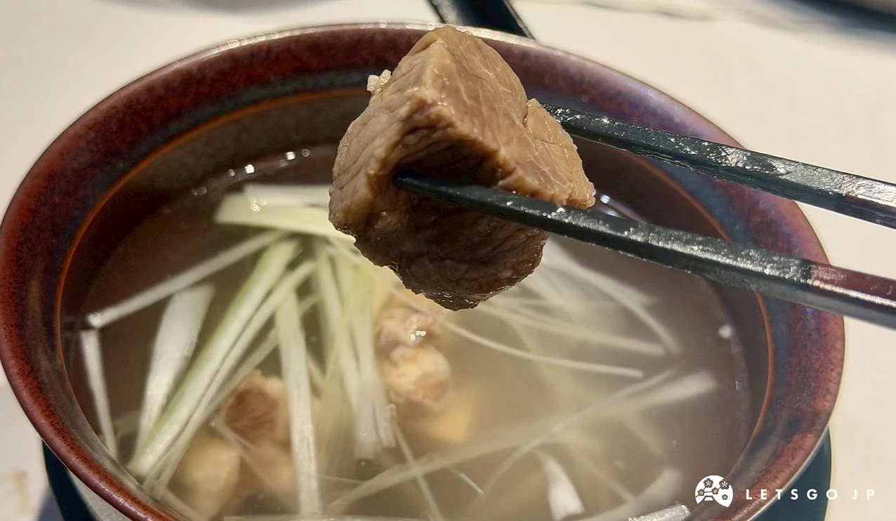 用筷子夾起牛尾湯中厚實飽滿的牛肉塊特寫,牛肉質地燉煮至軟嫩入味,湯頭清澈並撒上滿滿的鮮甜切絲青蔥。