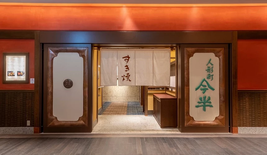 寫的「壽喜燒」日文字樣的布簾掛在店鋪門口上,右邊的牆壁上寫的「人形町今半」