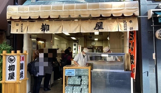 掛著白色寫著「柳屋」的布簾,有一位廚師在店門口櫃檯後,左邊有一個寫的柳屋的日式燈籠