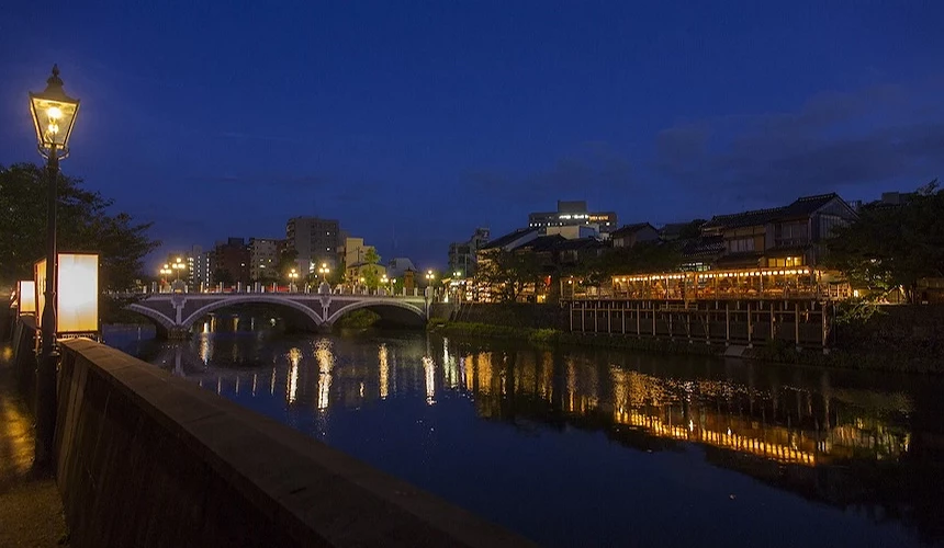 夜幕低垂河畔古镇,石桥与木造建筑灯火通明,倒影映于静水景致优美。
