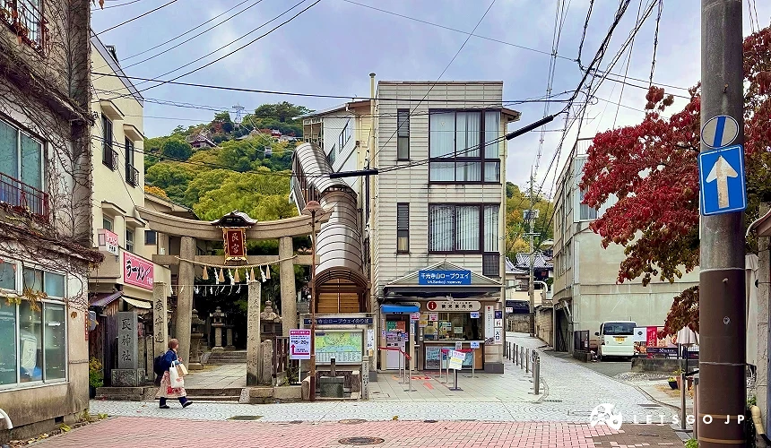 尾道艮神社入口,石造鸟居与参道位于街道旁,后方可见绿意山景。